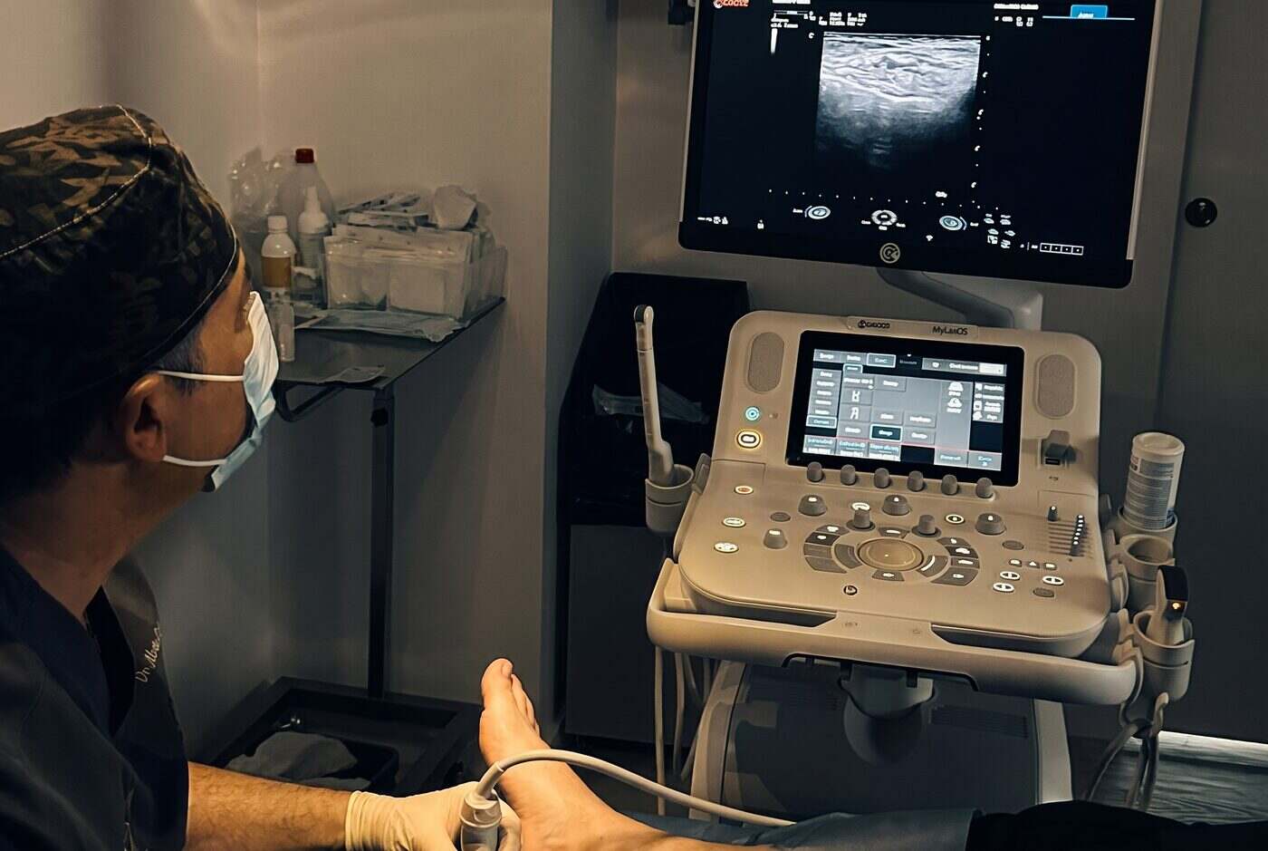 El Dr. Martín Rodríguez Banqueri realizando una infiltración ecoguiada en el pie de un paciente en Clínica Dolentia; en el monitor del ecógrafo, la imagen de ultrasonido que guía la aguja hasta la fascia plantar