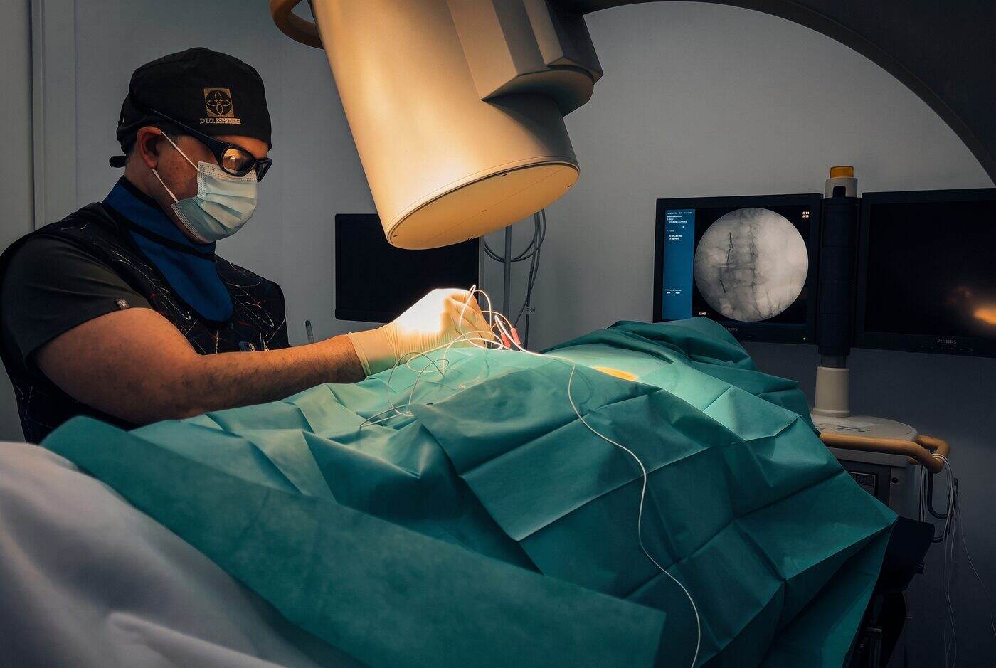 El Dr. Martín Rodríguez Banqueri colocando los electrodos de radiofrecuencia guiado por escopia sobre la columna de un paciente en Clínica Dolentia; en el monitor, la imagen radioscópica que confirma la posición de las agujas