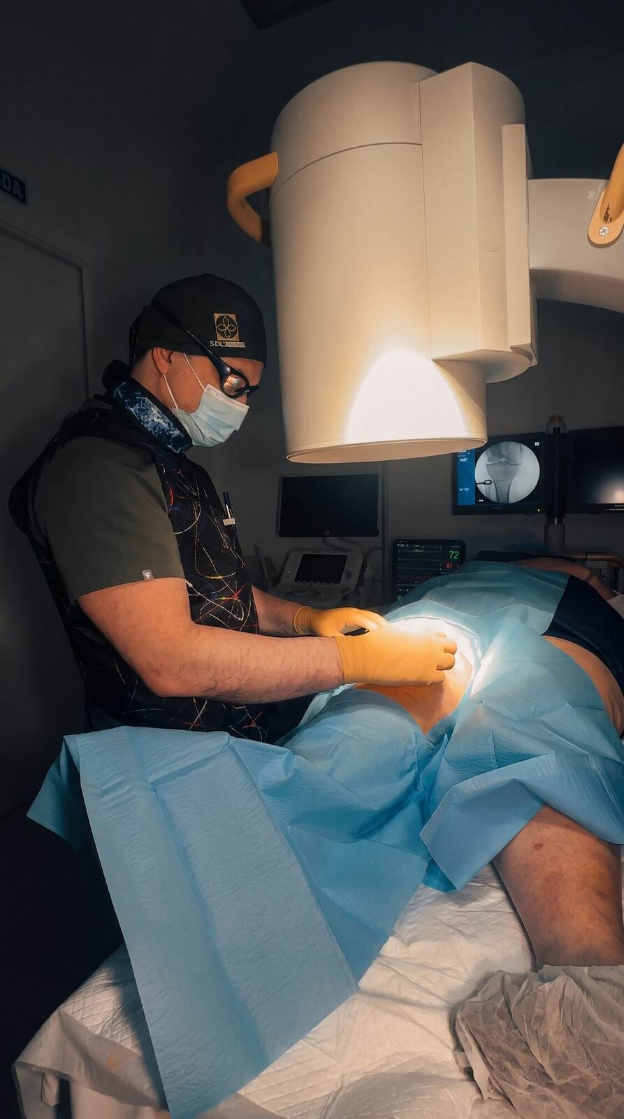 El Dr. Martín Rodríguez Banqueri infiltrando la rodilla guiado por escopia en la sala de intervencionismo de Clínica Dolentia; en el monitor, la imagen radioscópica de la articulación que guía la aguja