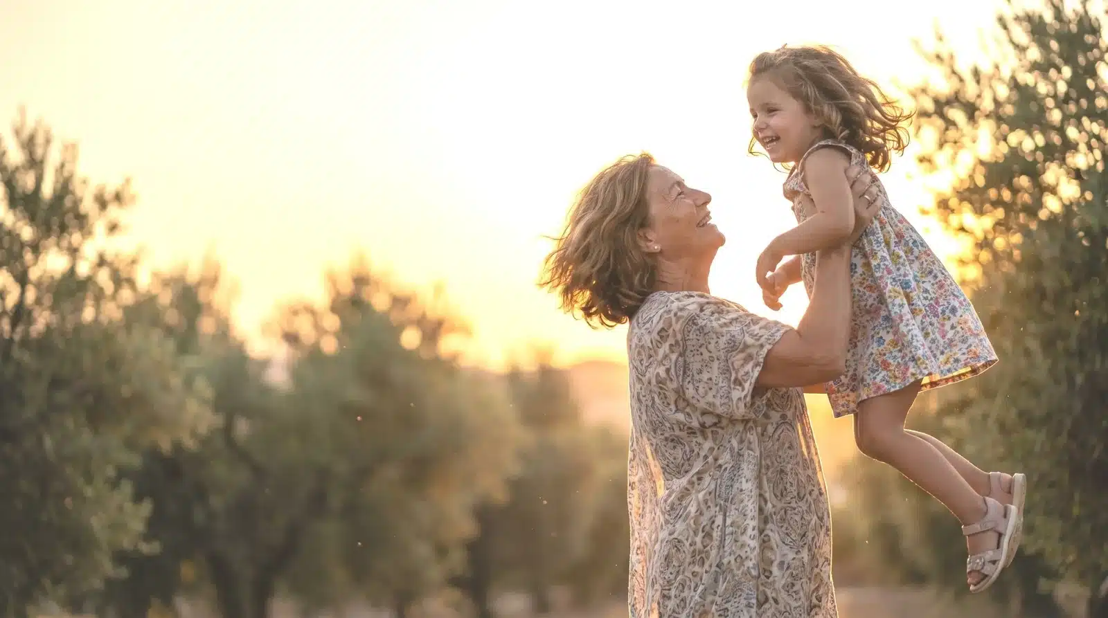 Abuela alzando a su nieta en un olivar al atardecer — la vida que el dolor te está quitando
